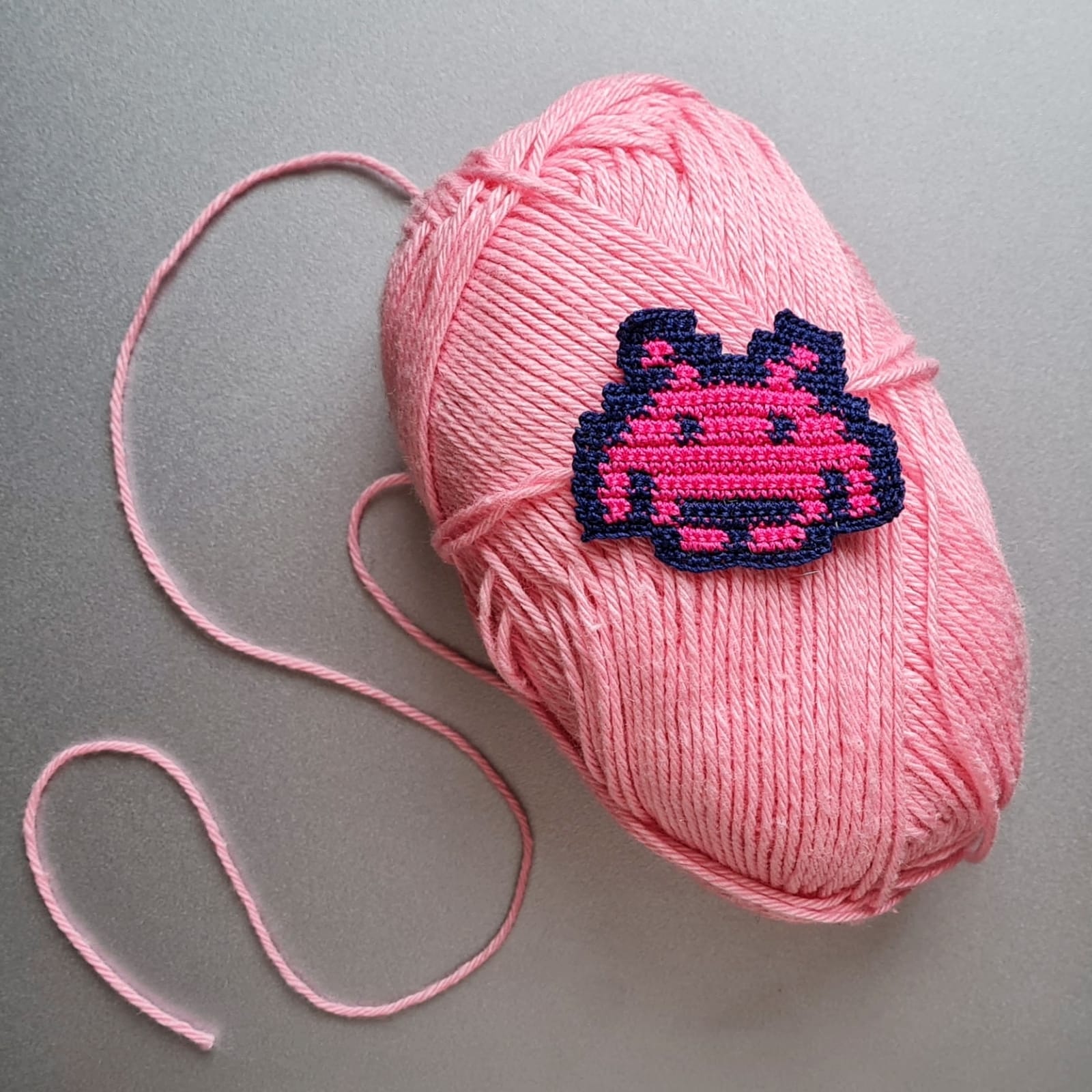 A crocheted space invader on a yarn ball.